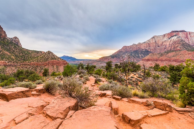 A scenic view of rugged red rock formations and desert vegetation under a cloudy sky.